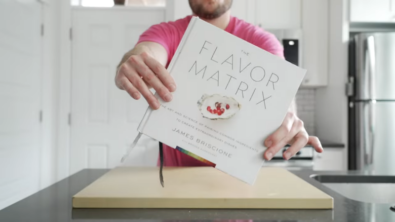 A Person Holding the Cookbook "The Flavor Matrix" by James Briscione in A Kitchen Setting