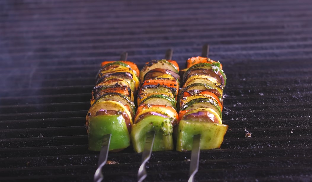 Colorful vegetable skewers, are grilling on a hot black surface