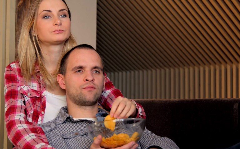 Couple relaxes on the couch, engrossed in a movie and sharing snacks