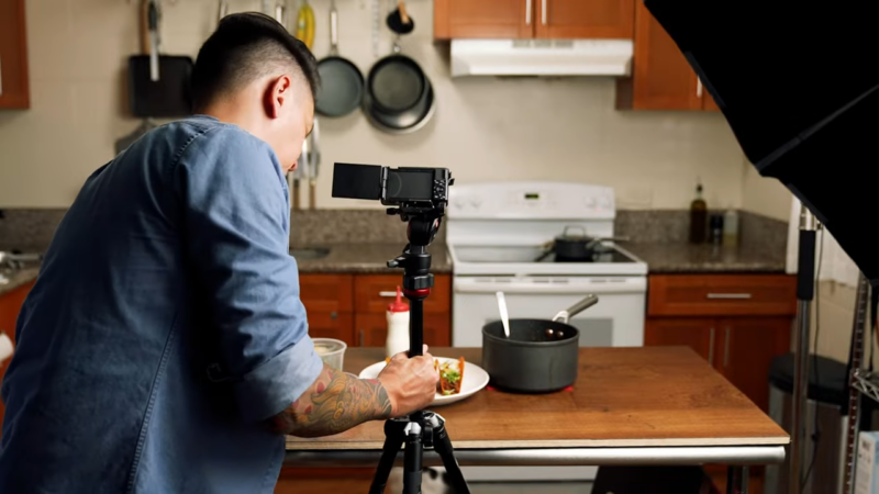 A Person Setting up A Camera on A Tripod to Film a Cooking Video in A Kitchen, Preparing the Final Dish for Filming