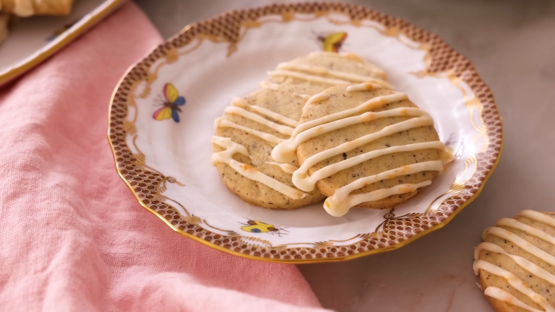 Two Buttery Earl Grey Cookies with Glaze Drizzle Are Served on A Decorative Plate Next to A Pink Cloth Napkin