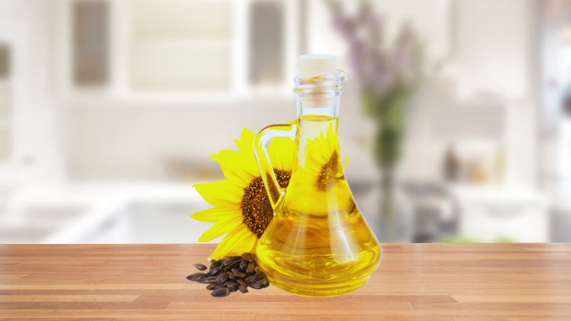 A Bottle of High-Oleic Sunflower Oil with Sunflower Seeds and A Sunflower Bloom Placed Next to It on A Wooden Surface