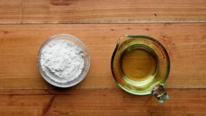 A glass bowl of flour and a measuring cup of vegetable oil sit side by side on a wooden surface, ready to make a roux