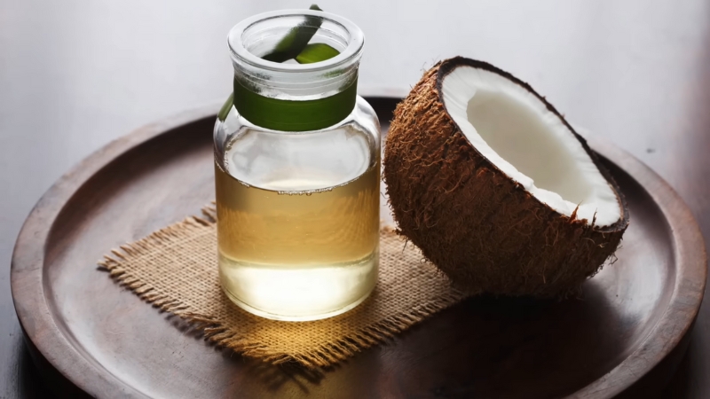 A Bottle of Refined Coconut Oil with A Coconut Half Placed Next to It on A Wooden Plate