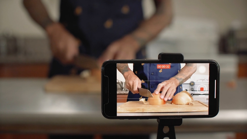 A person filming a cooking video of themselves chopping an onion with a smartphone on a tripod
