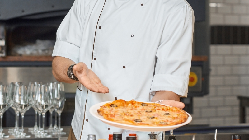 A chef presents a freshly made pizza, capturing the hands-on learning style seen in beginner-friendly cooking shows
