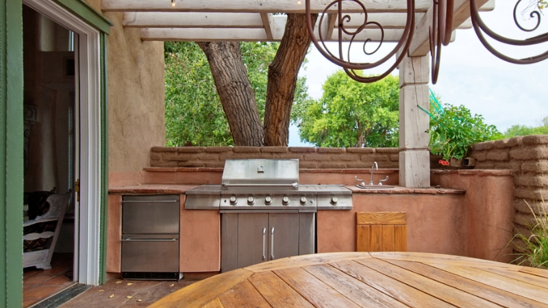 Outdoor kitchen setup with a built-in grill, sink, and counter space under a shaded pergola in a backyard patio area
