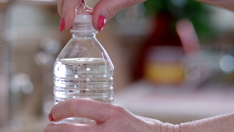 A person opening a plastic water bottle illustrates how bottled and spring water can impact coffee taste at home