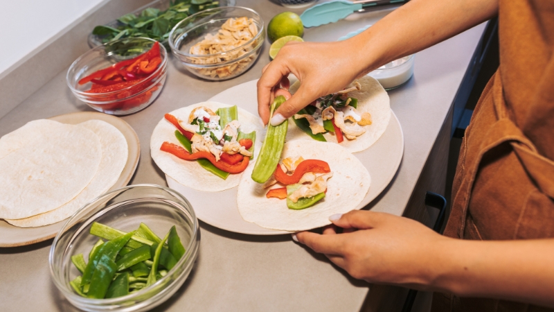 A person arranges fresh vegetables and chicken in tortillas, making the dish look Instagram-ready