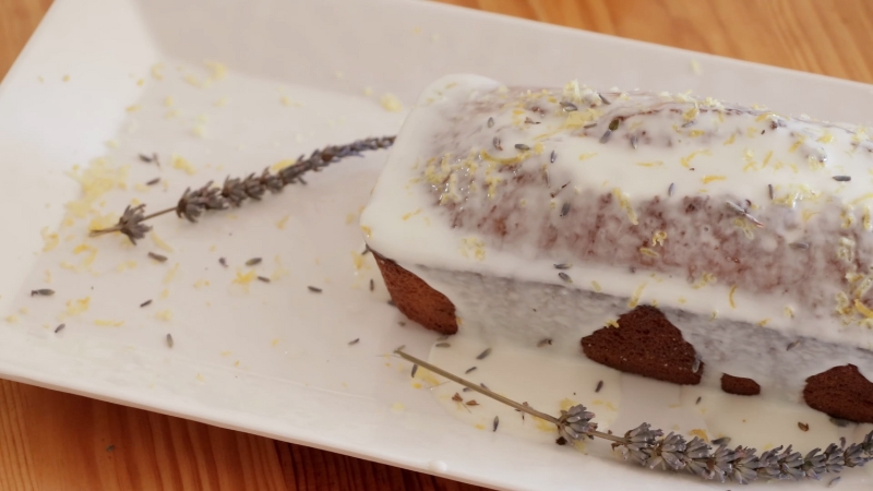 Lemon lavender loaf cake topped with a white lemon glaze, garnished with dried lavender buds and lemon zest on a white serving platter