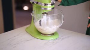 A stand mixer blending batter in a glass bowl on a kitchen counter