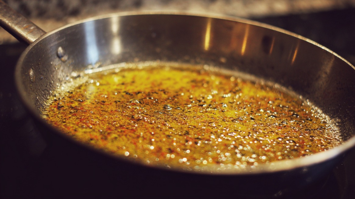 Close-up of melted butter and seasoning bubbling in a stainless steel frying pan