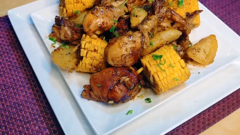 A plate of roasted chicken pieces with corn and potatoes garnished with chopped herbs