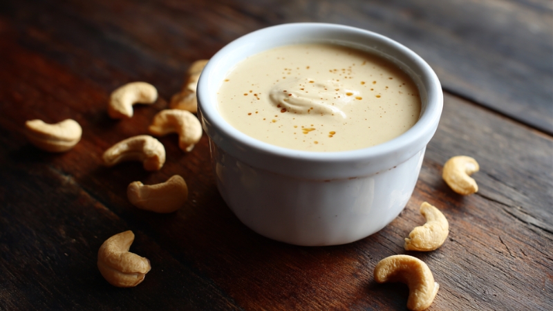 Creamy vegan cashew sauce served in a small white bowl surrounded by raw cashews