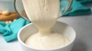 Smooth cashew sauce being poured from a blender into a white bowl