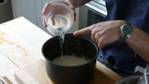 Water being poured into a pot of rinsed rice in a rice cooker insert before cooking
