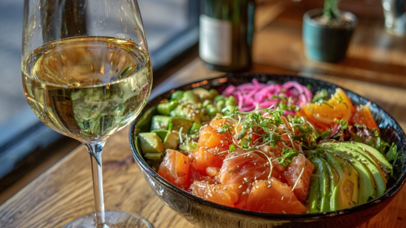 A vibrant lox poke bowl served alongside a glass of chilled white wine, highlighting a fresh and elegant pairing