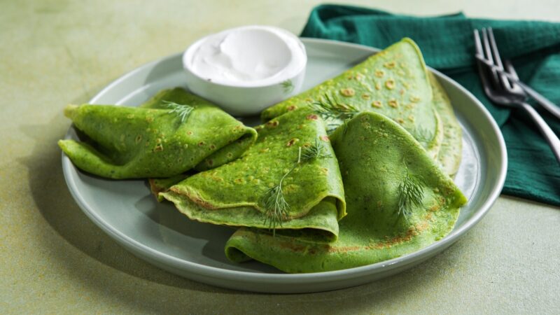 Green spinach pancakes with yogurt dip sit on a plate