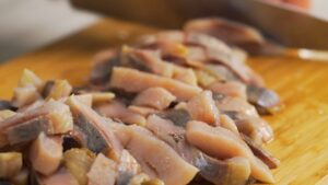 Sliced pickled herring pieces on a wooden cutting board