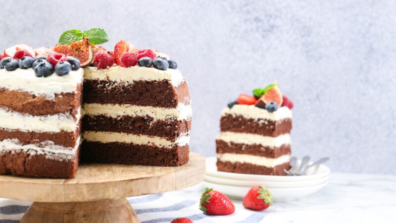 Chocolate layer cake with cream and fresh berries sits beside a plated slice