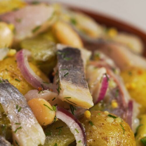 Pickled herring salad with potatoes, red onion, pickles, and fresh herbs in a serving bowl