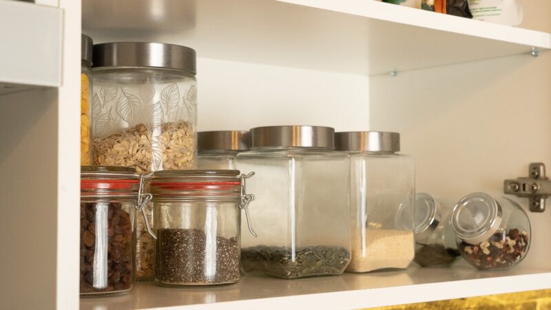 Glass jars with dry pantry items sit on a white kitchen shelf